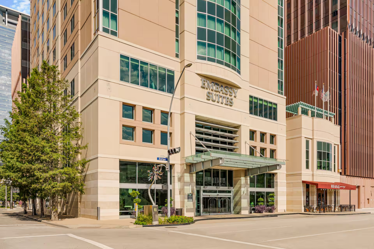 Exterior of a modern hotel, "Embassy Suites," with tall beige walls and green-tinted windows.