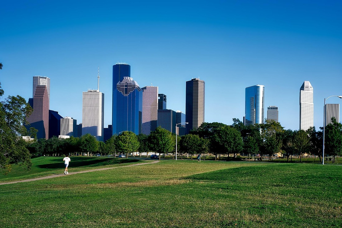 The downtown skyline of Houston, Texas. A man runs on a path through green space in the foreground.