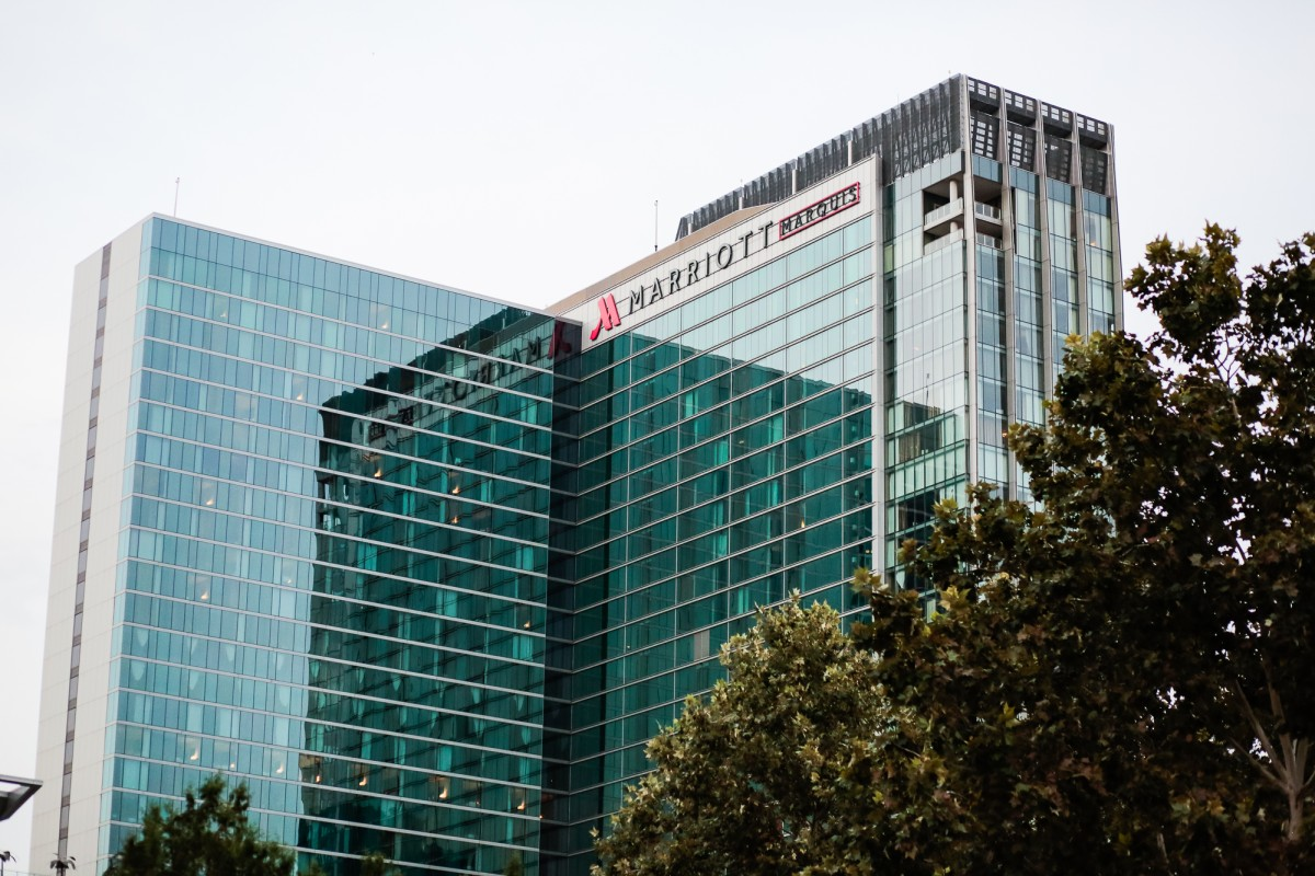 A modern high-rise building with a glass facade, displaying the Marriott Marquis logo on top.