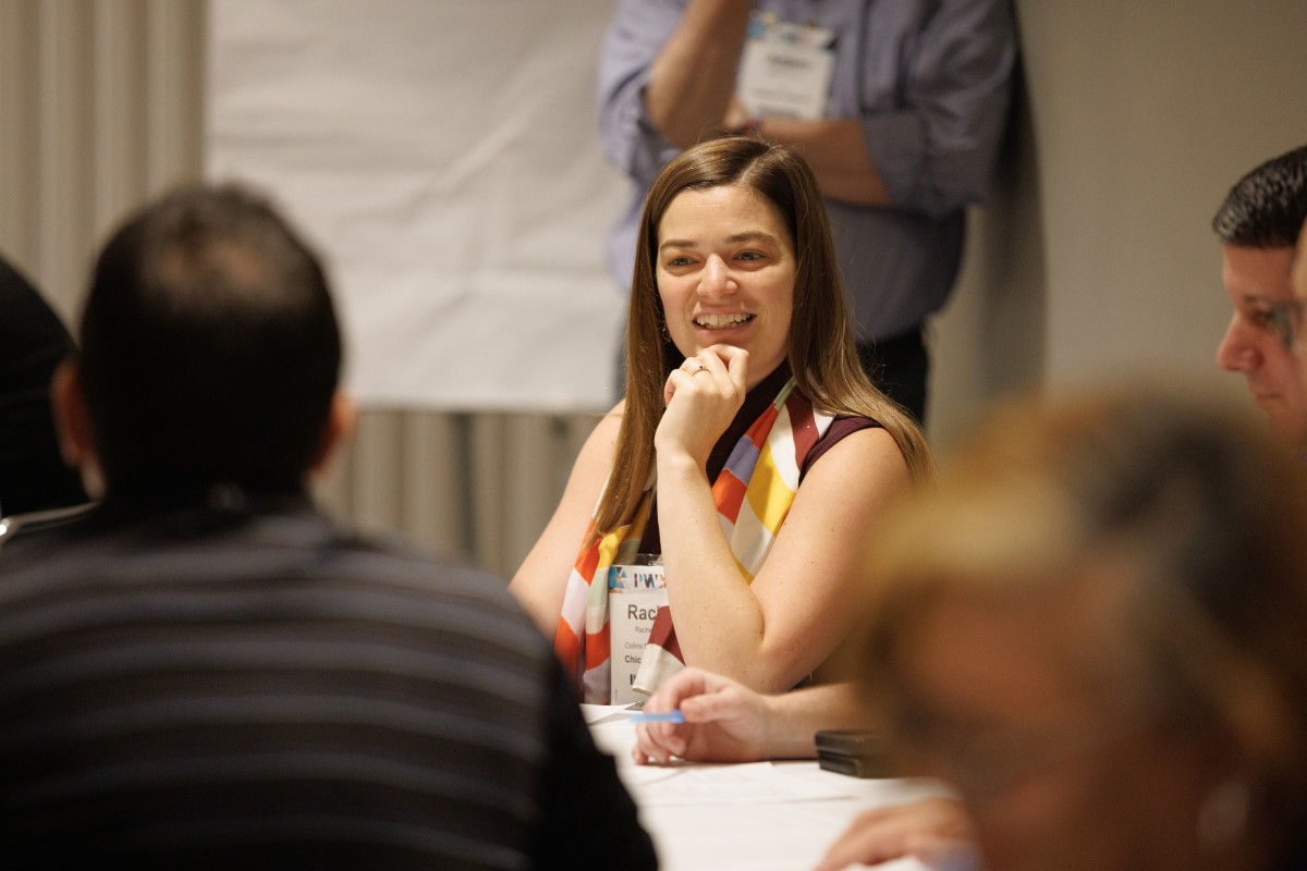 A woman smiles in a group discussion around a conference table as part of the Solution Hub at PWX.