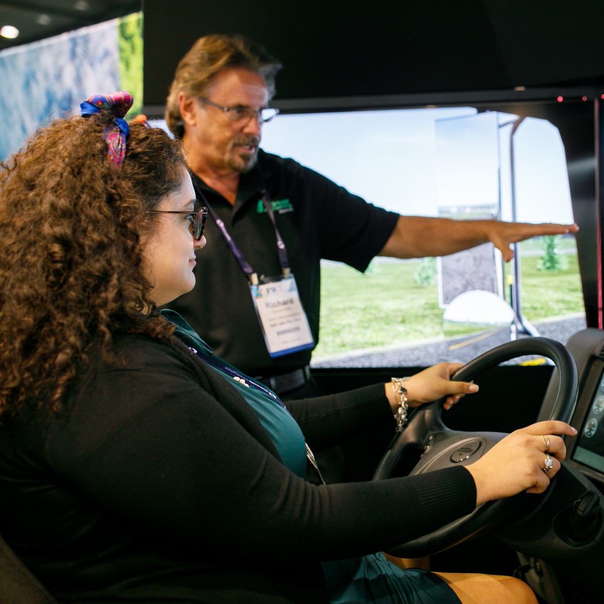 A PWX exhibitor looks on as an attendee operates a driving simulator.