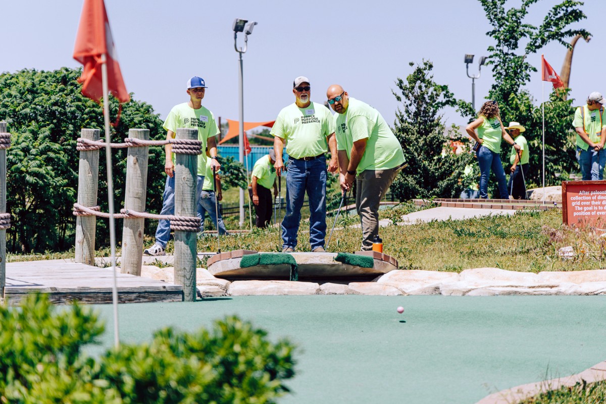 Three men in matching green t-shirts play mini golf.