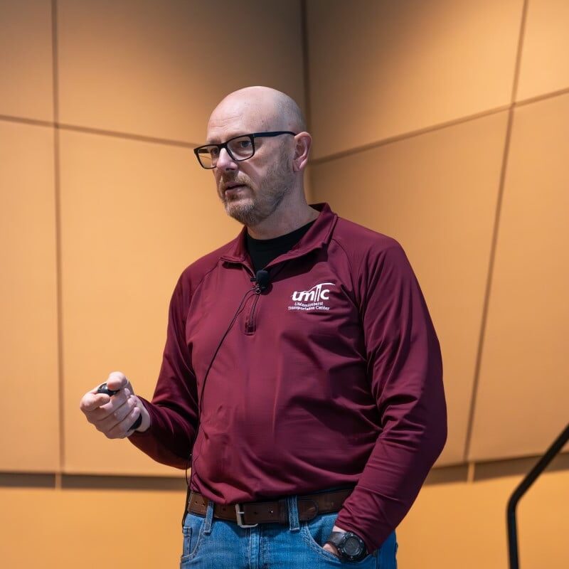 A man in glasses and a maroon shirt speaks at an education session.