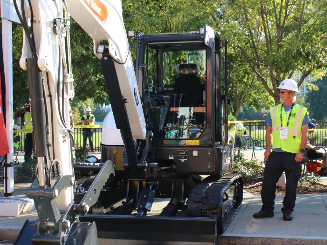 a public works professional stands next to an excavator